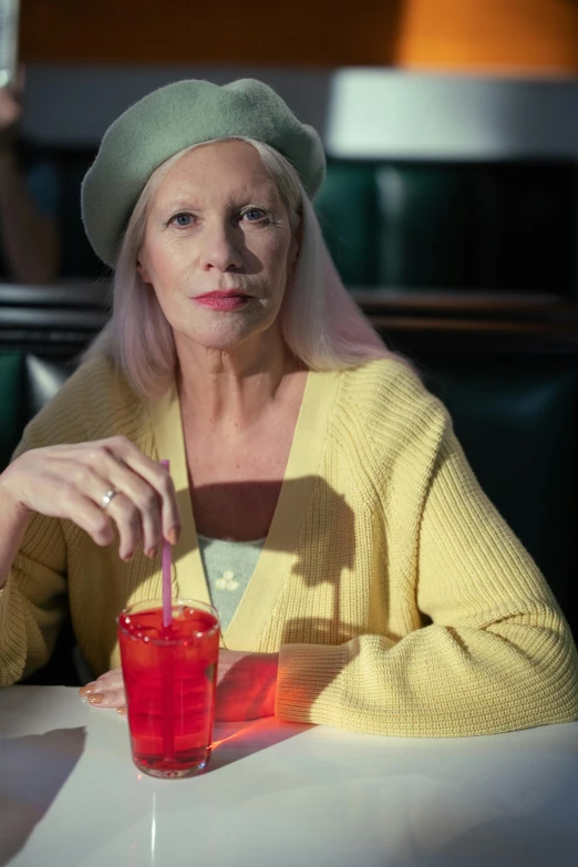 a woman sitting at a table with a drink, a colorized photo, by Lee Gatch, trending on pexels, photorealism, intense albino, pink iconic character, humans of new york style, older woman