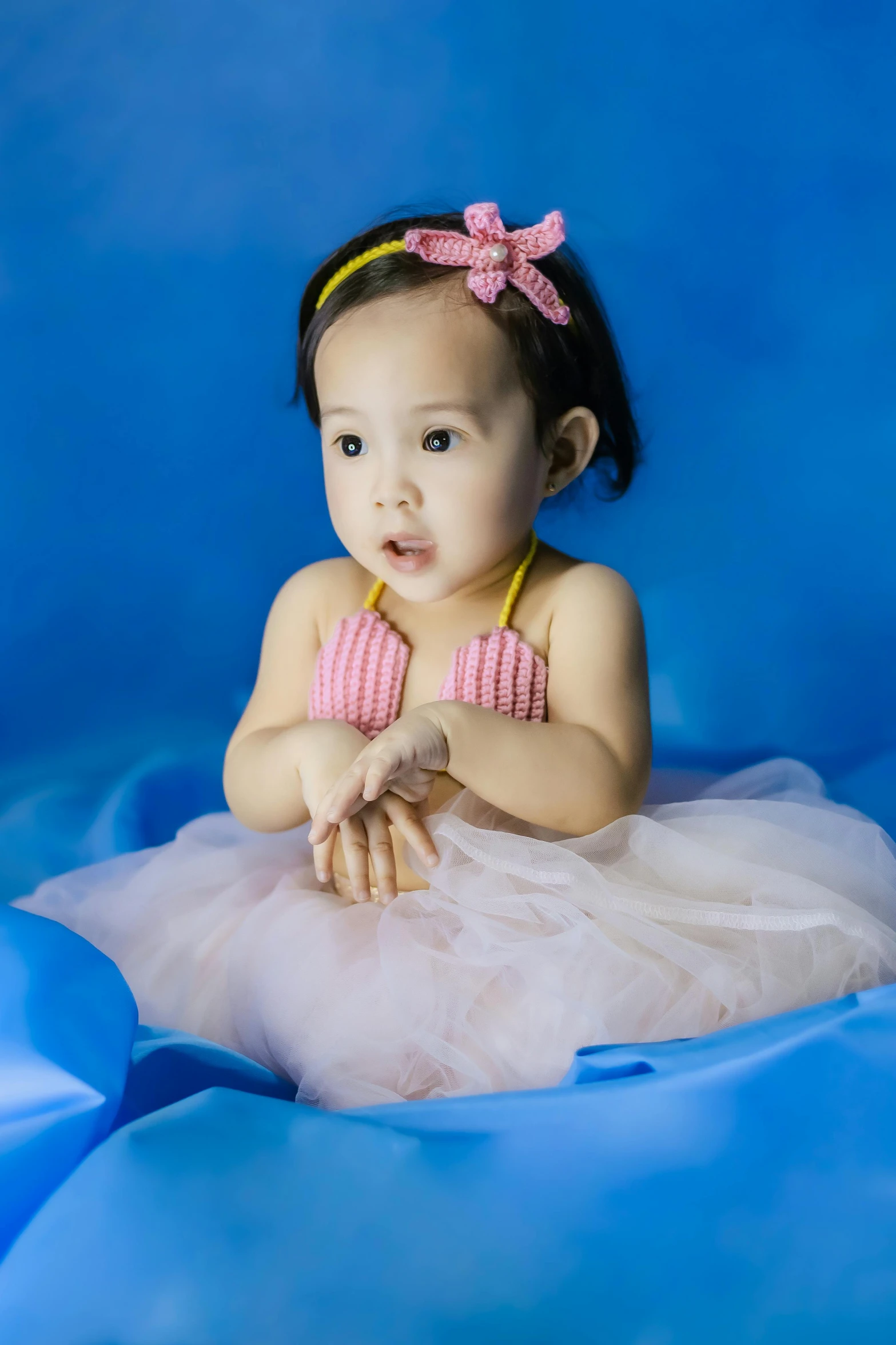 a little girl sitting on top of a blue blanket, wearing a pink tutu, wearing seashell attire, blue background colour, slide show