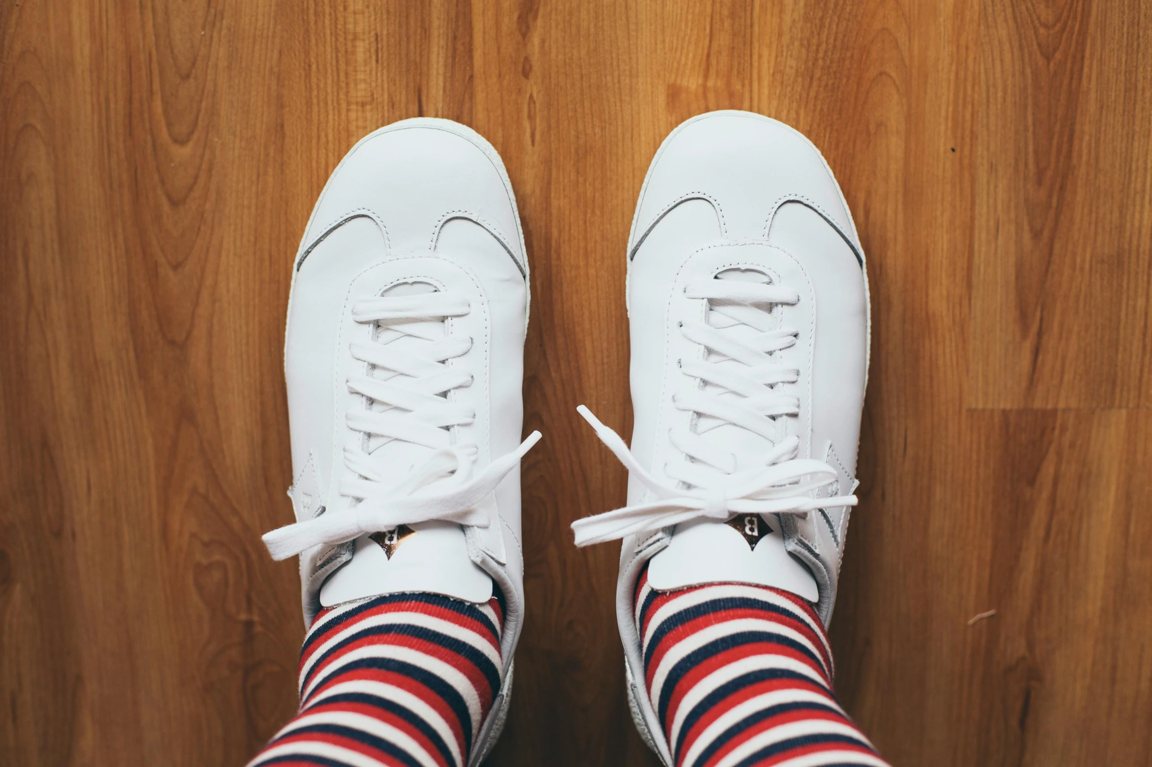 a pair of white sneakers sitting on top of a wooden floor, by Julia Pishtar, trending on pexels, striped pantyhose, patriotic, white soft leather model, non-binary