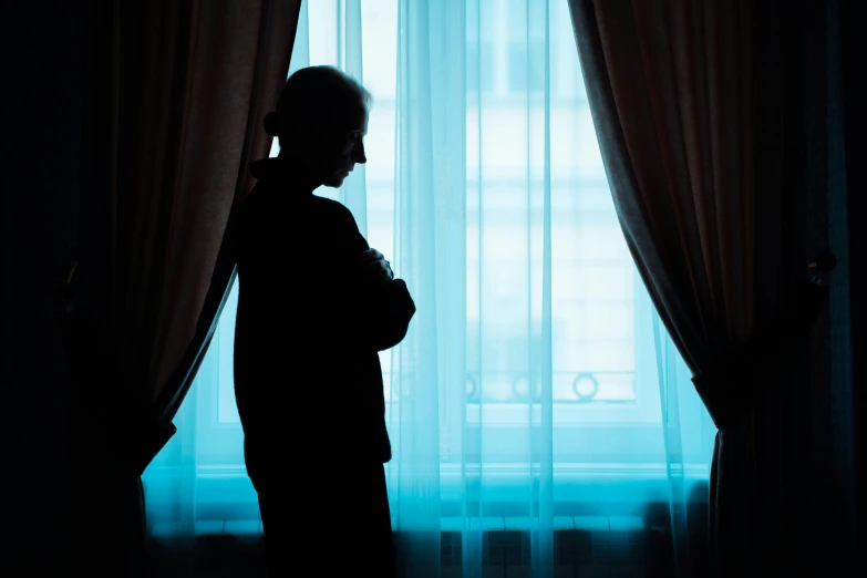 a silhouette of a man standing in front of a window, dementia, curtains, she's sad, an oldman