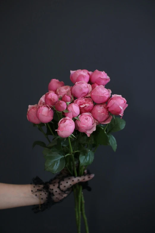 a person holding a bunch of pink roses, inspired by Pierre-Joseph Redouté, unsplash, with a black background, on a gray background, covered with pink marzipan, black peonies