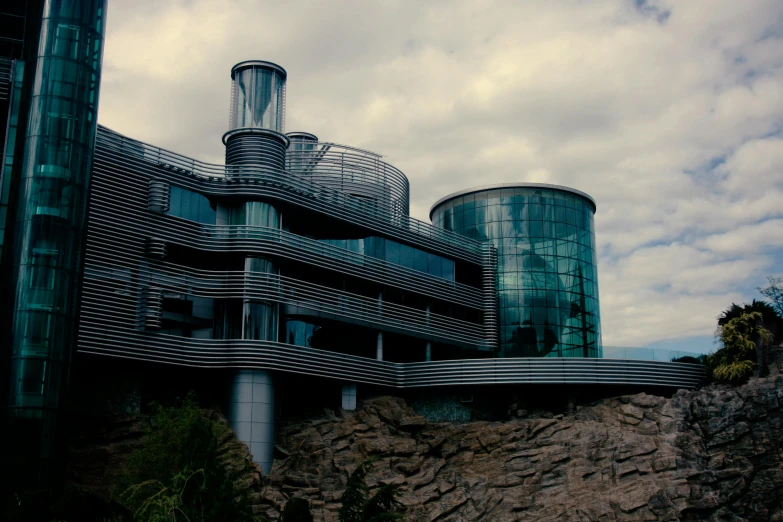 a large building sitting on top of a lush green hillside, inspired by Ned M. Seidler, unsplash, art nouveau, glass and steel, сastle on the rock, albuquerque, gloomy skies
