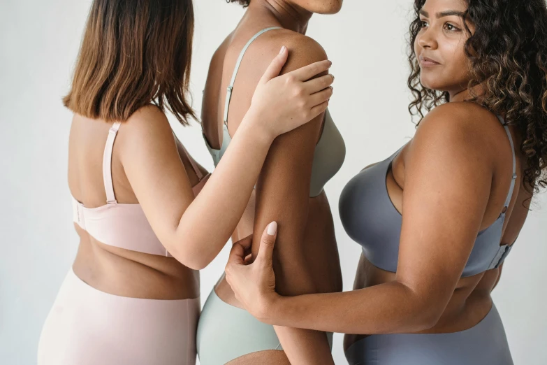 three women in underwear standing next to each other, trending on unsplash, muted arm colors, showing curves, colourised, woman holding another woman