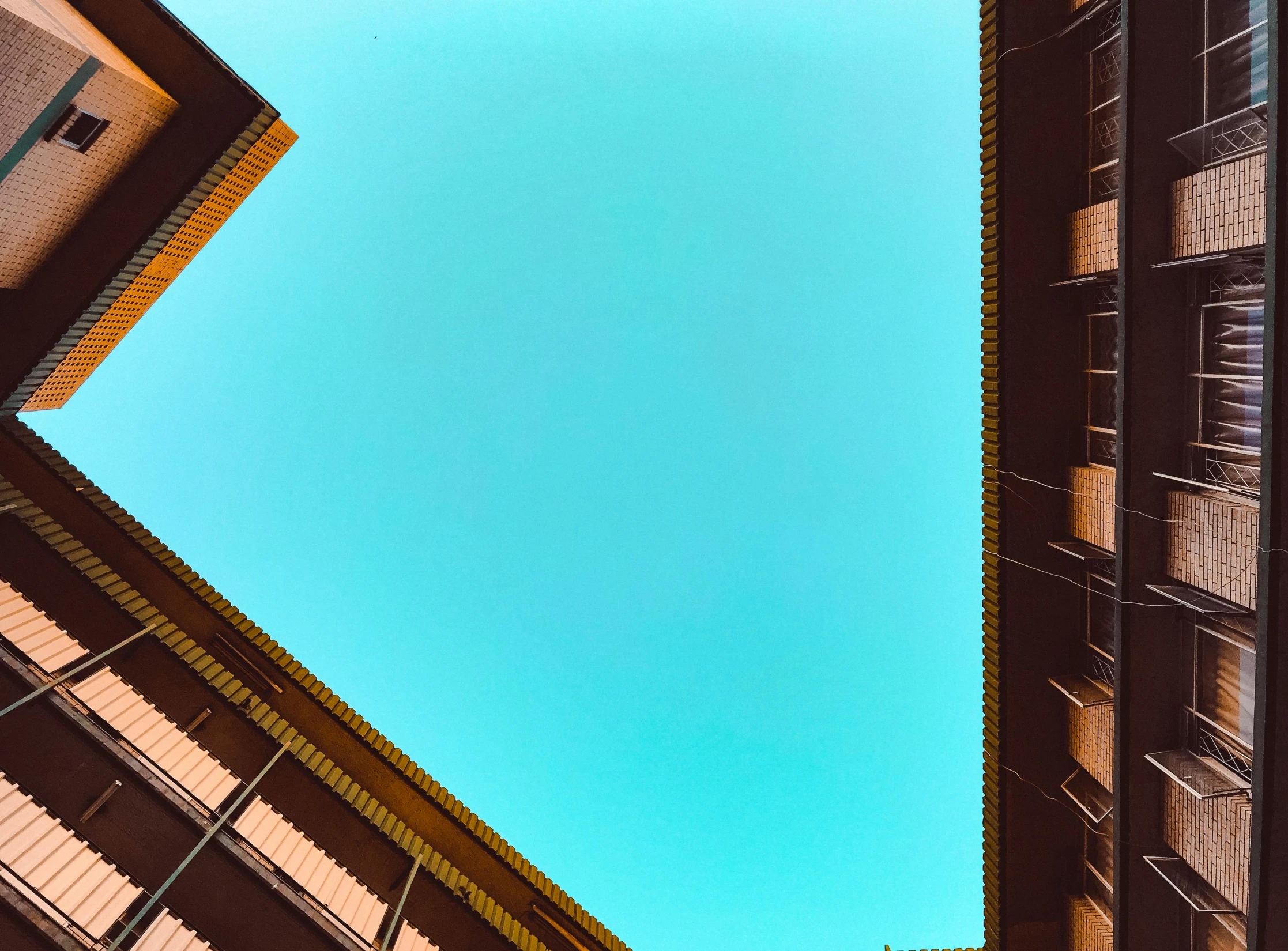 a very tall building with a blue sky in the background, an album cover, by Kristian Zahrtmann, pexels contest winner, minimalism, brown and cyan color scheme, roofs, view from below, outside intricate