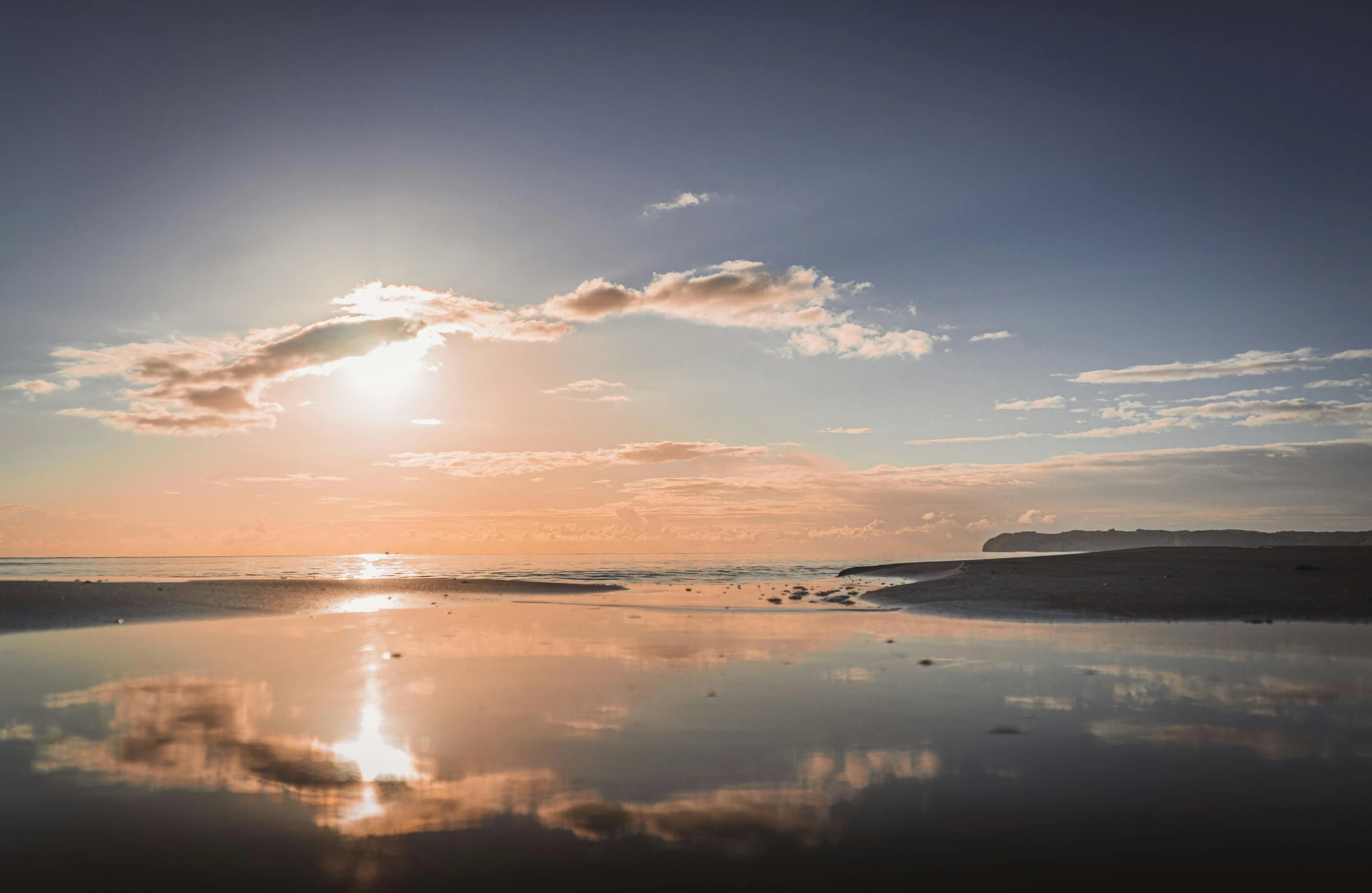 a person riding a surfboard on top of a sandy beach, it is sunset, reflection in the water, iceland photography, golden bay new zealand