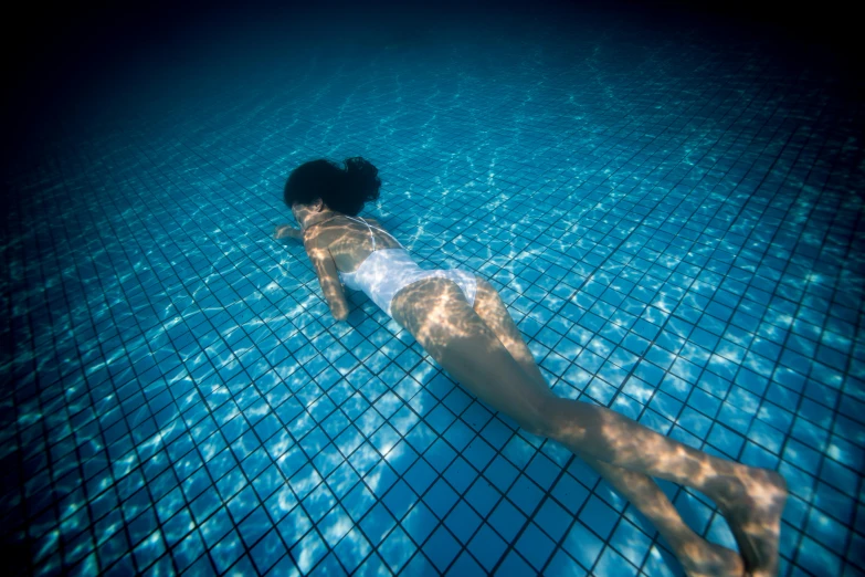 a woman swimming under water in a pool, inspired by Elsa Bleda, fan favorite, closed swimsuit, checkerboard pattern underwater, translucent