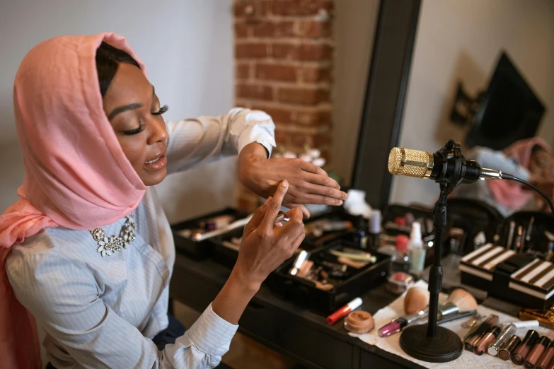 a woman putting on makeup in front of a mirror, by Everett Warner, pexels contest winner, hurufiyya, hijab, alexis franklin, hands on counter, on set