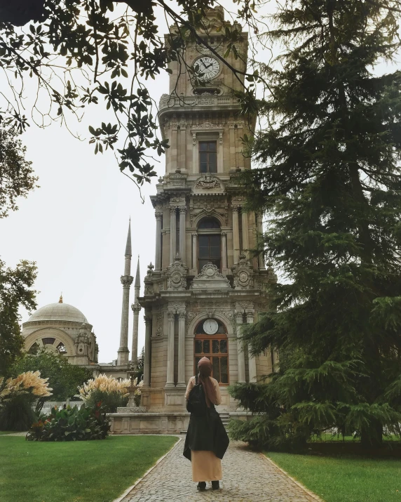 a woman standing in front of a clock tower, inspired by Niyazi Selimoglu, pexels contest winner, exterior botanical garden, 1910s architecture, raden saleh, instagram picture