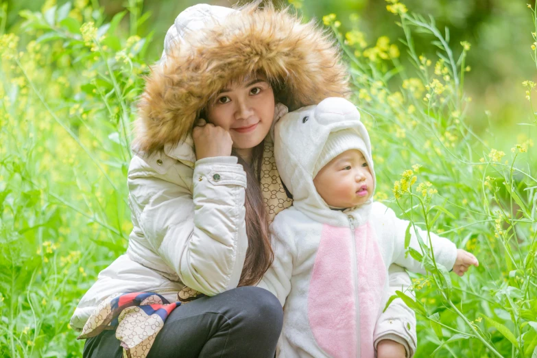 a woman sitting next to a baby in a field, inspired by Kate Greenaway, pexels, action shot girl in parka, hangzhou, fur hood, 1505