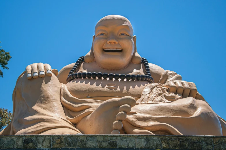 a statue of a laughing buddha in front of a blue sky, a statue, by Meredith Dillman, joyful smirk, asian, shaved temple, brown