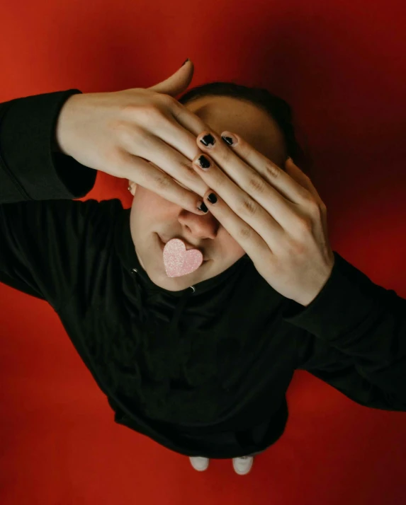 a woman sticking her tongue out with her hands, an album cover, by Attila Meszlenyi, trending on pexels, aestheticism, glass sculpture of a heart, androgynous male, snacks, pink and red colors