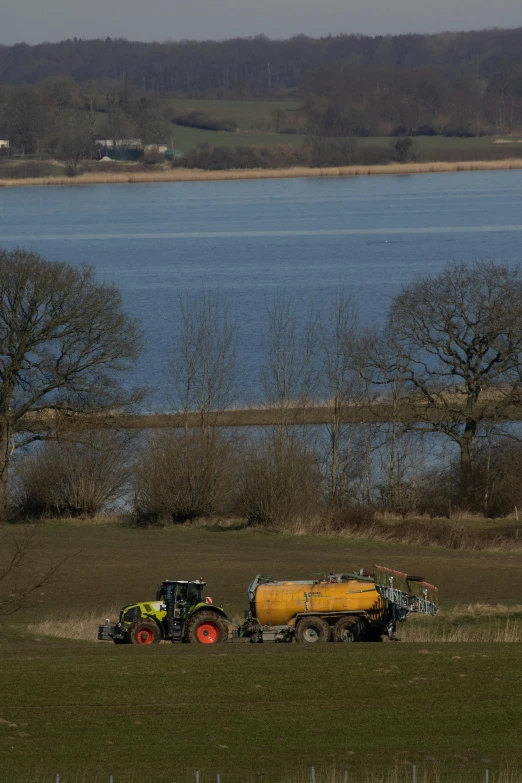 a couple of tractors that are in the grass, a picture, by Colin Middleton, land art, lake in the distance, photographed for reuters, thumbnail, spraying liquid