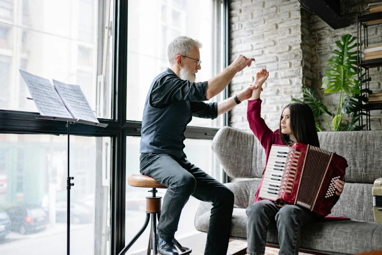 a man and a woman sitting on a couch playing an accordion, pexels contest winner, hurufiyya, little kid, teaching, thumbnail, next to a big window