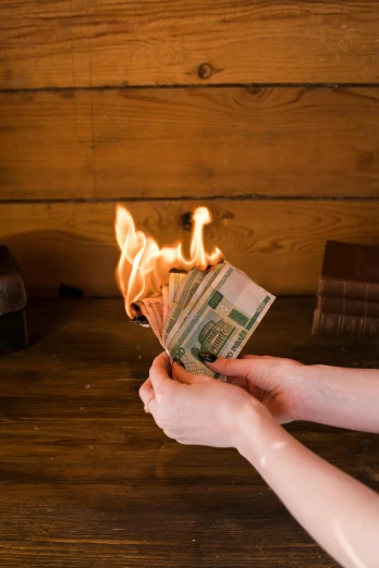 a person holding a stack of money in front of a fire, pexels contest winner, renaissance, pissed off, jen atkin, on a wooden desk, politics