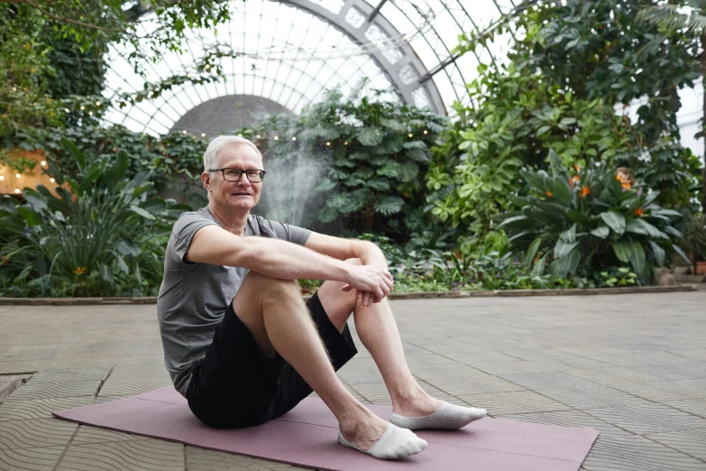a man sitting on top of a yoga mat, inspired by Graham Forsythe, standing in a botanical garden, man with glasses, 5 5 yo, biodome