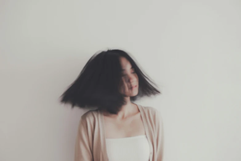 a woman standing in front of a white wall, by Shang Xi, unsplash, realism, messy black bob hair, on a pale background, hair blowing, indoor picture