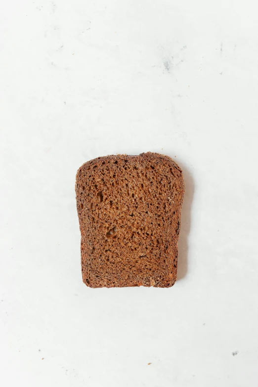 a piece of bread sitting on top of a white surface, a portrait, unsplash, battle toast, dark brown, reddish, sandstone