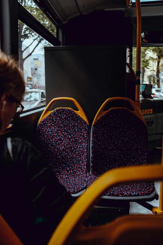 a woman sitting on a bus looking out the window, by Nathalie Rattner, unsplash, black and yellow and red scheme, sitting in a wheelchair, spotted, 🚿🗝📝