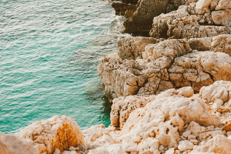 a man standing on top of a cliff next to the ocean, by Emma Andijewska, pexels contest winner, corals are gemstones, white travertine terraces, middle close up shot, ((rocks))