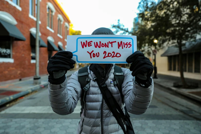 a person holding a sign that says we won't miss you 2020, pexels, pulitzer prize winning photo, wintermute, back facing, instagram post