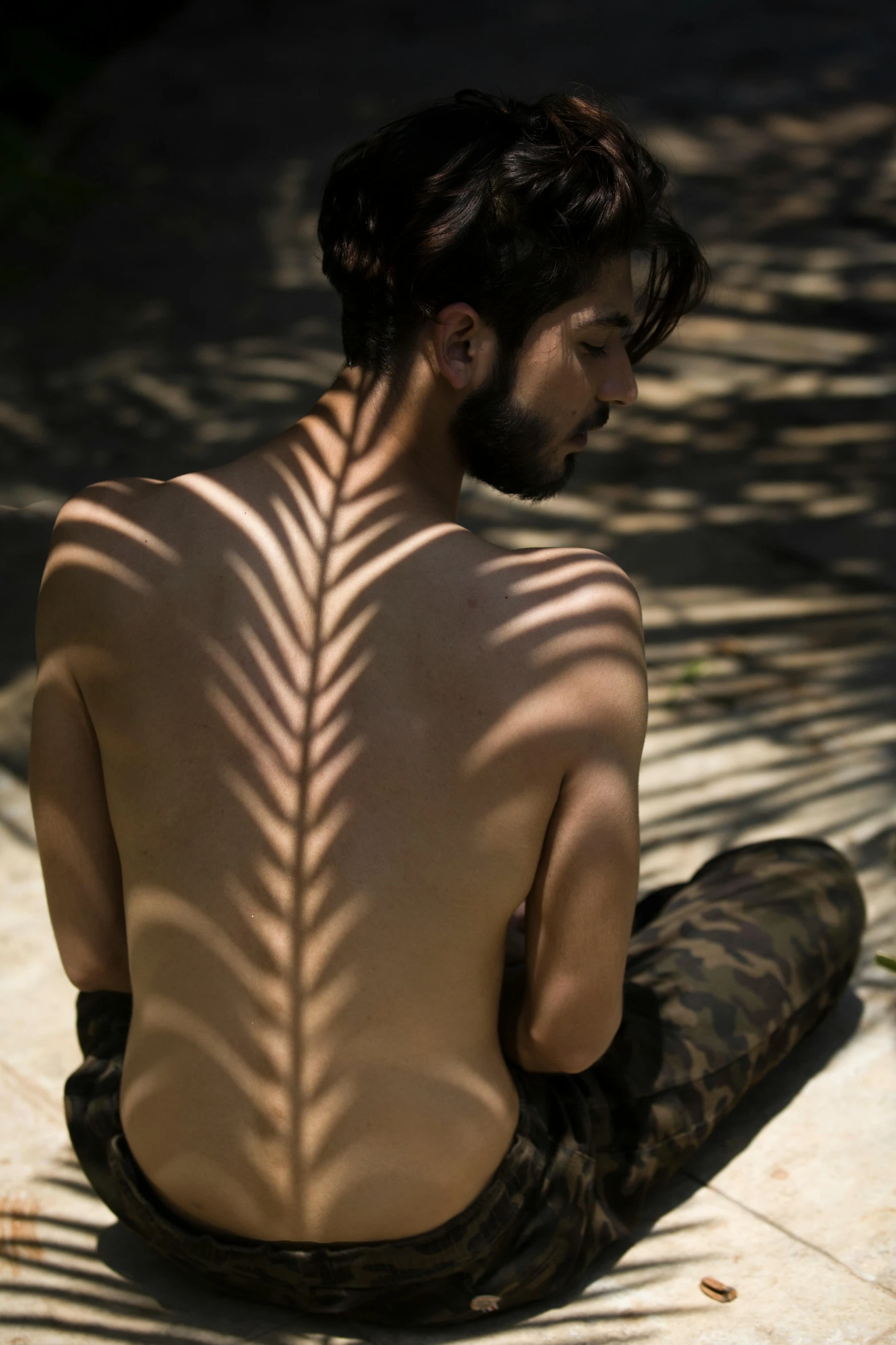 a man sitting on the ground with his back to the camera, inspired by Byron Galvez, sunlight filtering through skin, palm lines, person made of tree, showing her shoulder from back