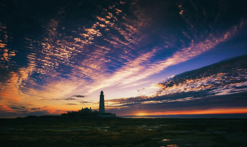 a lighthouse sitting on top of a sandy beach, by Bertram Brooker, unsplash contest winner, glowing nacreous clouds, yorkshire, hazy sunset with dramatic clouds, instagram post