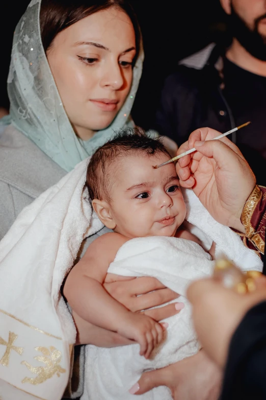 a priest is feeding a baby with a spoon, a colorized photo, by Julia Pishtar, pexels contest winner, hurufiyya, eyebrows, acupuncture treatment, turban, with infant jesus