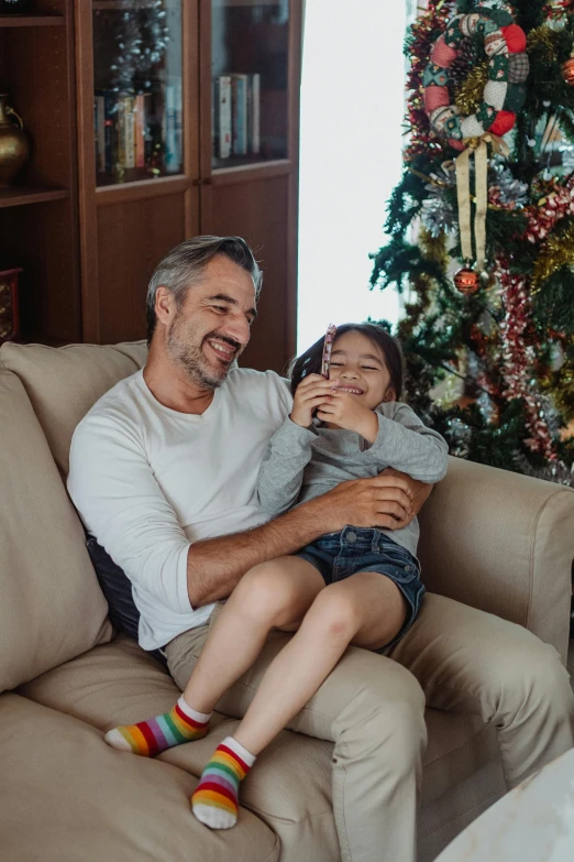 a man and a little girl sitting on a couch in front of a christmas tree, lgbtq, straya, gray men, thumbnail