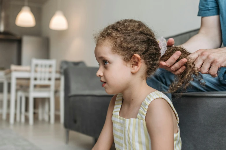 a woman combing a little girl's hair while sitting on a couch, pexels contest winner, incoherents, curly bangs and ponytail, looking from shoulder, local conspirologist, over his shoulder