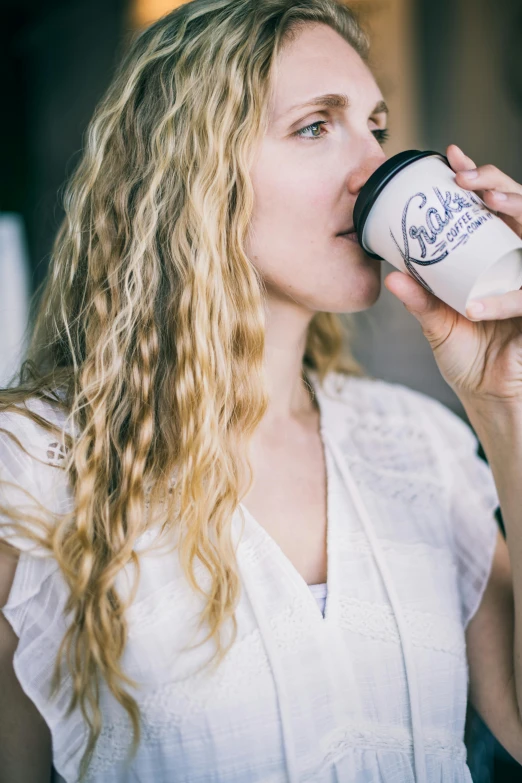 a woman drinking out of a coffee cup, unsplash, happening, long curly light blond hair, holding a bottle, cait miers, celebration of coffee products