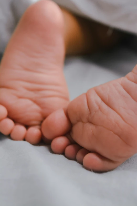 a close up of a baby's feet on a bed, by Dan Christensen, pexels, symbolism, promo image, hatched ear, different sizes, boys