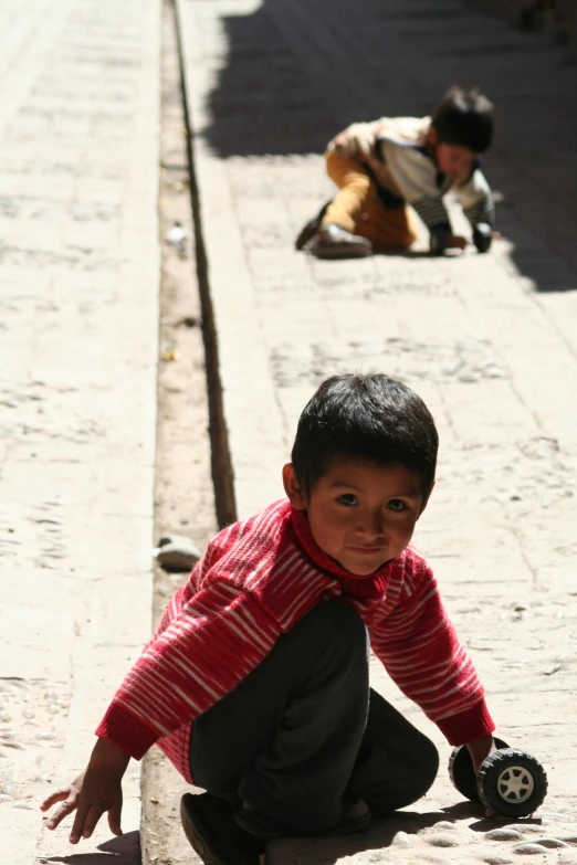 a young boy riding a skateboard down a street, inspired by Steve McCurry, quito school, sitting on the floor, quechua!, small in size, with his back turned