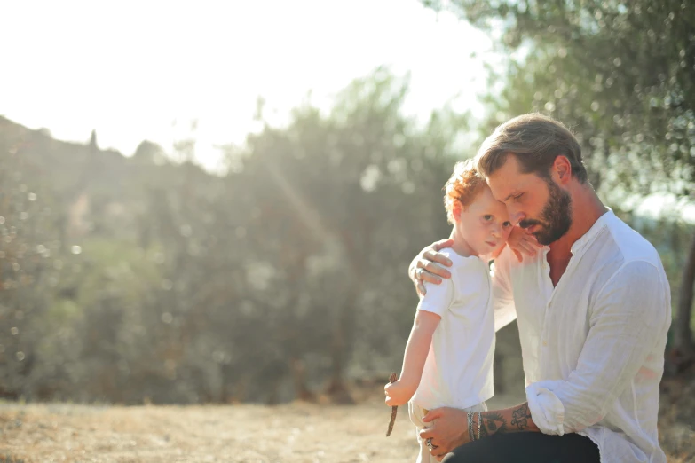 a man kneeling down holding a small child, a portrait, by Romain brook, pexels, summer light, bearded, white, 15081959 21121991 01012000 4k