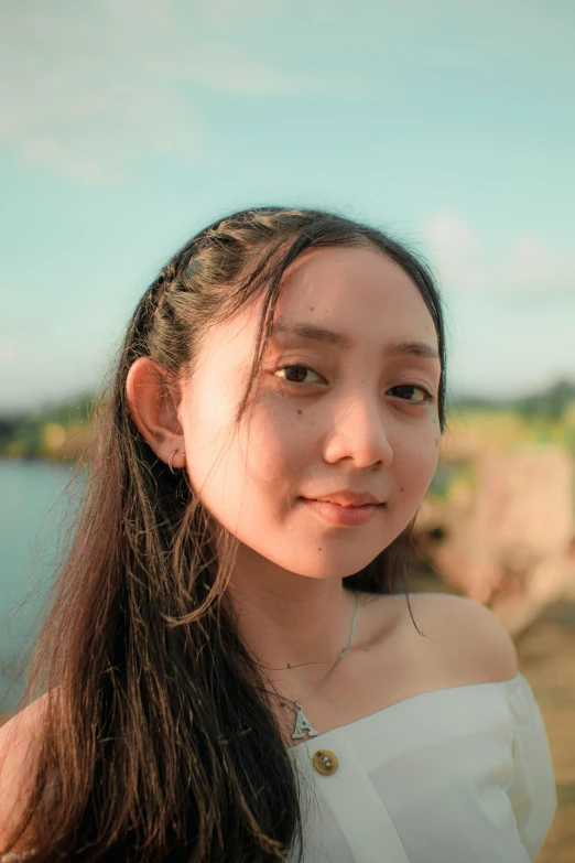 a woman standing in front of a body of water, an album cover, inspired by Ai Xuan, pexels contest winner, realism, headshot profile picture, lovingly looking at camera, discord profile picture, in the evening