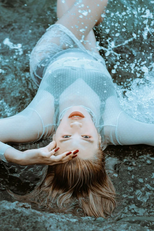 a woman laying on the ground in the water, inspired by Elsa Bleda, unsplash contest winner, renaissance, transparent gray dress, wet look, sydney sweeney, metallic cyan bodysuit