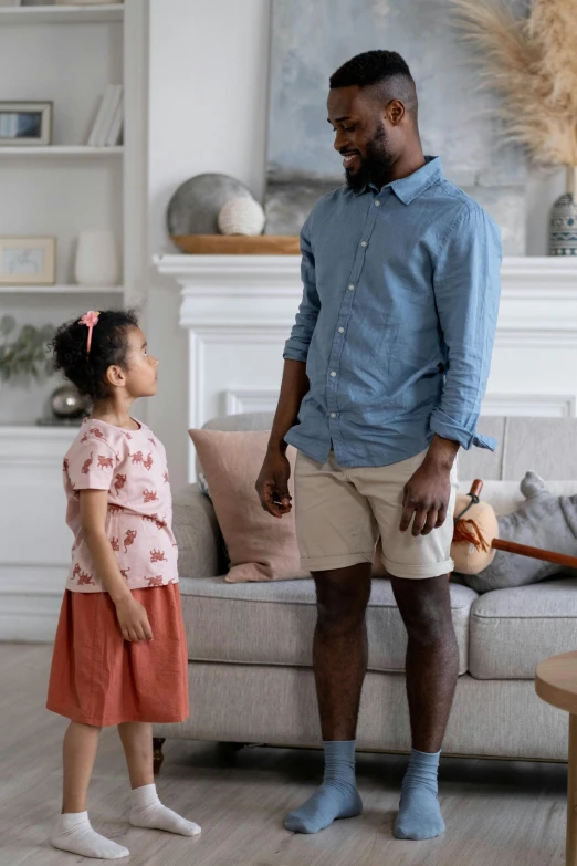 a man standing next to a little girl in a living room, diverse outfits, commercial, khakis, talking