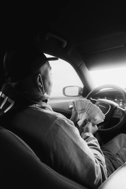 a man sitting in the driver's seat of a car, a black and white photo, by Andrew Stevovich, pexels contest winner, dollar bills, hip hop aesthetic, delivering mail, playboi carti