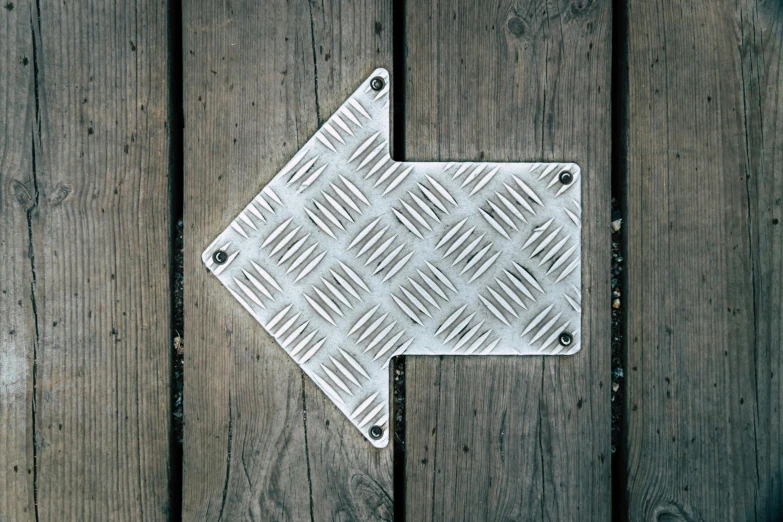 a close up of a metal arrow on a wooden floor, unsplash, square, metal plate photograph, patterned, white steel