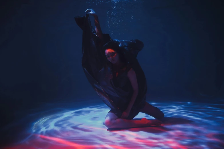 a woman sitting on the ground under water, an album cover, unsplash contest winner, conceptual art, red and blue black light, woman in black robes, performing a music video, float