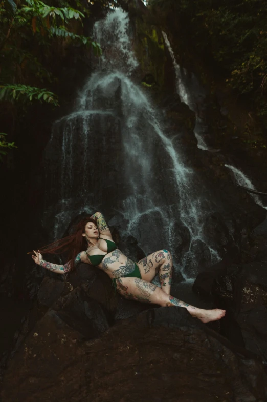 a woman laying on a rock in front of a waterfall, inspired by Elsa Bleda, renaissance, fully tattooed body, samoan features, full body tattoo, album