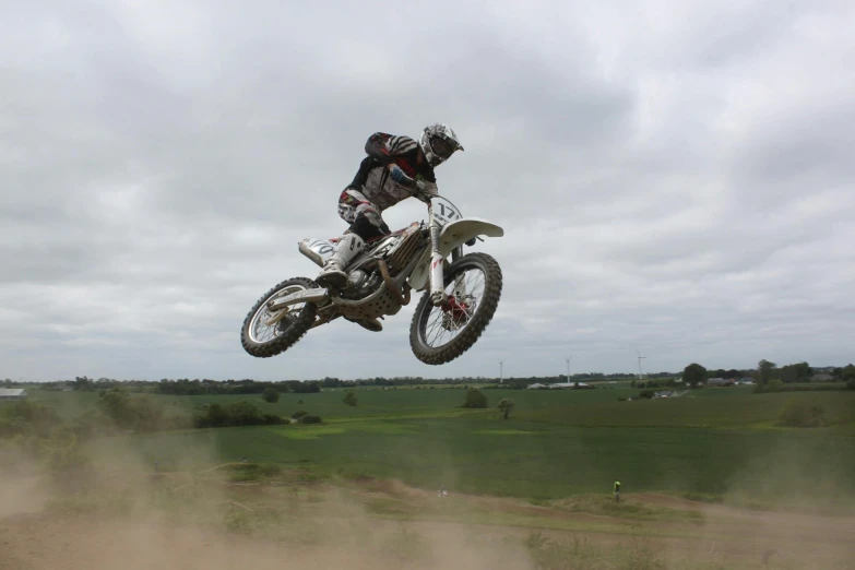 a man flying through the air while riding a dirt bike, grey, helmet off, white, vapour