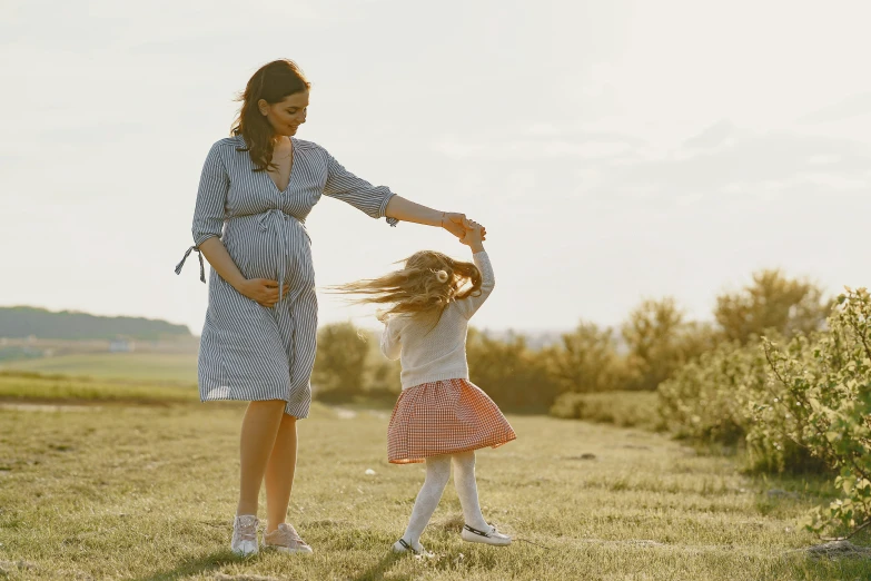 a woman standing next to a little girl in a field, pexels contest winner, symbolism, pregnant belly, she is dancing, thumbnail, walking to the right