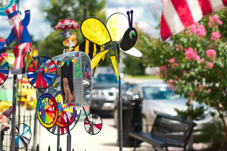 a row of wind sculptures sitting on the side of a road, a portrait, flickr, painting big bees flying around, bentonville arkansas, colorful scene, carousel