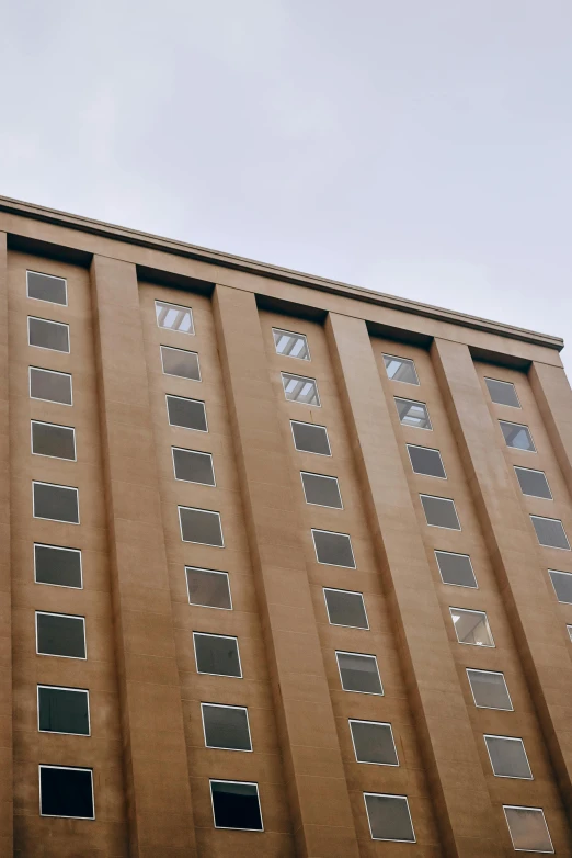 a tall brown building with lots of windows, inspired by Donald Judd, unsplash, low quality photo, light - brown wall, bottom view ， bladerunner, william warehouse