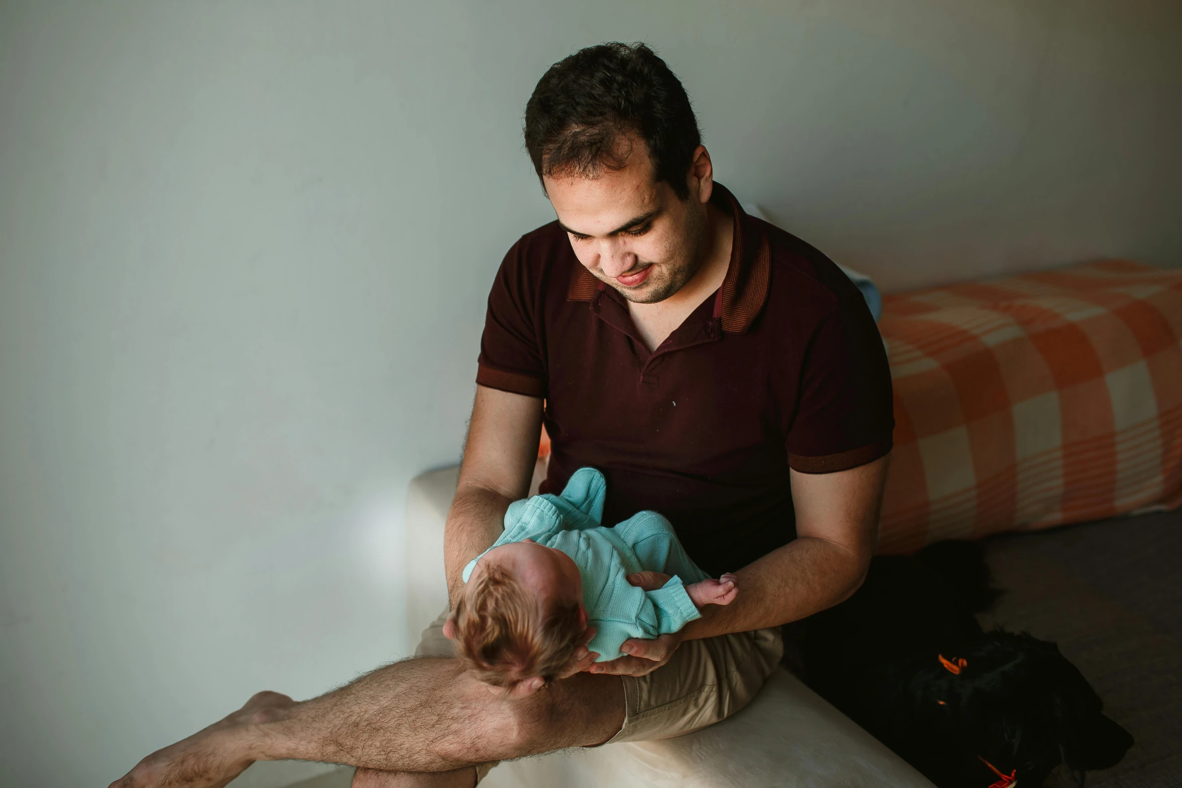 a man sitting on a bed holding a baby, pexels contest winner, avatar image, spanish, 1 2 9 7, brown