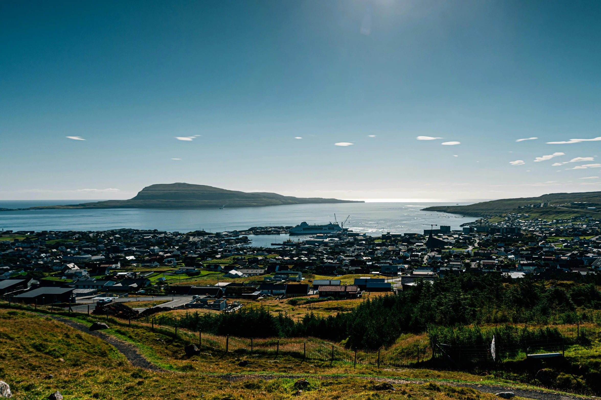 a large body of water sitting next to a lush green hillside, by Hallsteinn Sigurðsson, pexels contest winner, hurufiyya, town in the background, the harbour at stromness orkney, solar eclipse in iceland, panoramic view