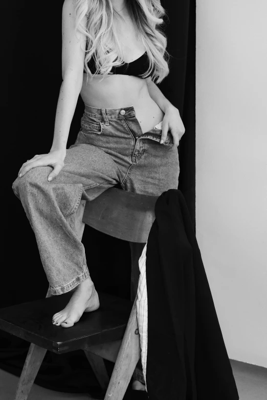 a black and white photo of a woman sitting on a stool, a black and white photo, unsplash, photorealism, baggy jeans, model エリサヘス s from acquamodels, physical : tinyest midriff ever, ✨🕌🌙