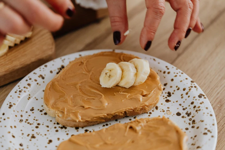 a white plate topped with peanut butter and banana slices, inspired by Richmond Barthé, trending on pexels, manuka, hands on counter, blond, thumbnail