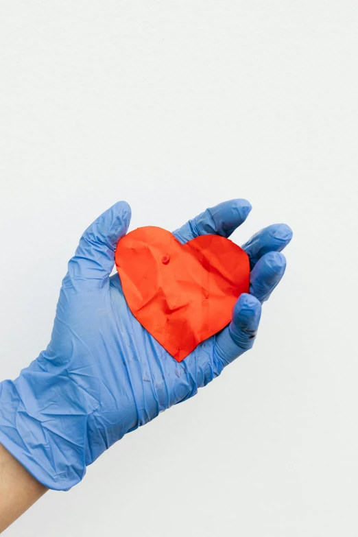 a person in blue gloves holding a red heart, plasticien, made of lab tissue, made from paper, silicone skin, orange