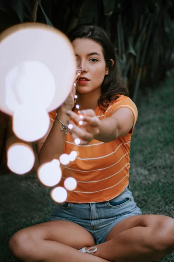 a woman sitting on the ground holding a light bulb, pexels contest winner, light and space, hanging out with orbs, looking into a mirror, 5 0 0 px models, orange hue